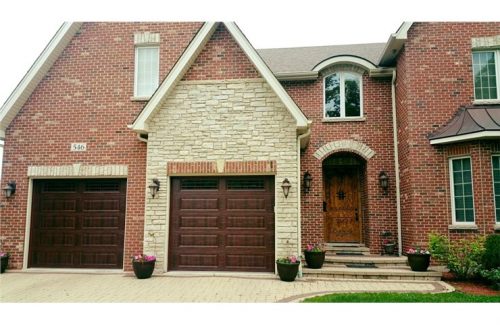 brown wooden garage doors on large brick house